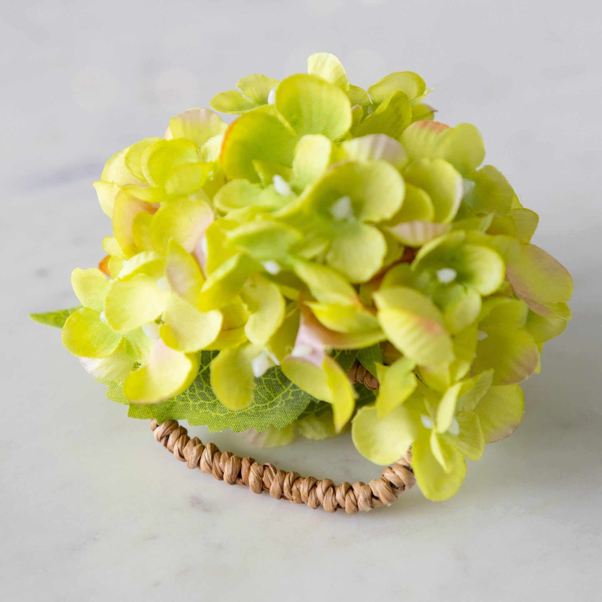 Green Hydrangea Napkin Ring with a rattan ring, on a marble surface.