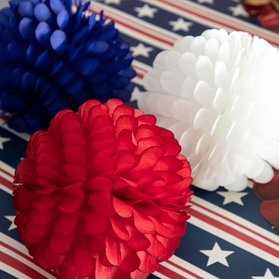 Three Hester &amp; Cook patriotic ruffled balls, set of 3, on a table.