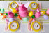 Easter-themed table setting with honeycomb bunnies, eggs and carrots decorations, Spring Plaid Placemats, colorful plates, pink napkins and gold flatware on the Green Awning Stripe Runner.