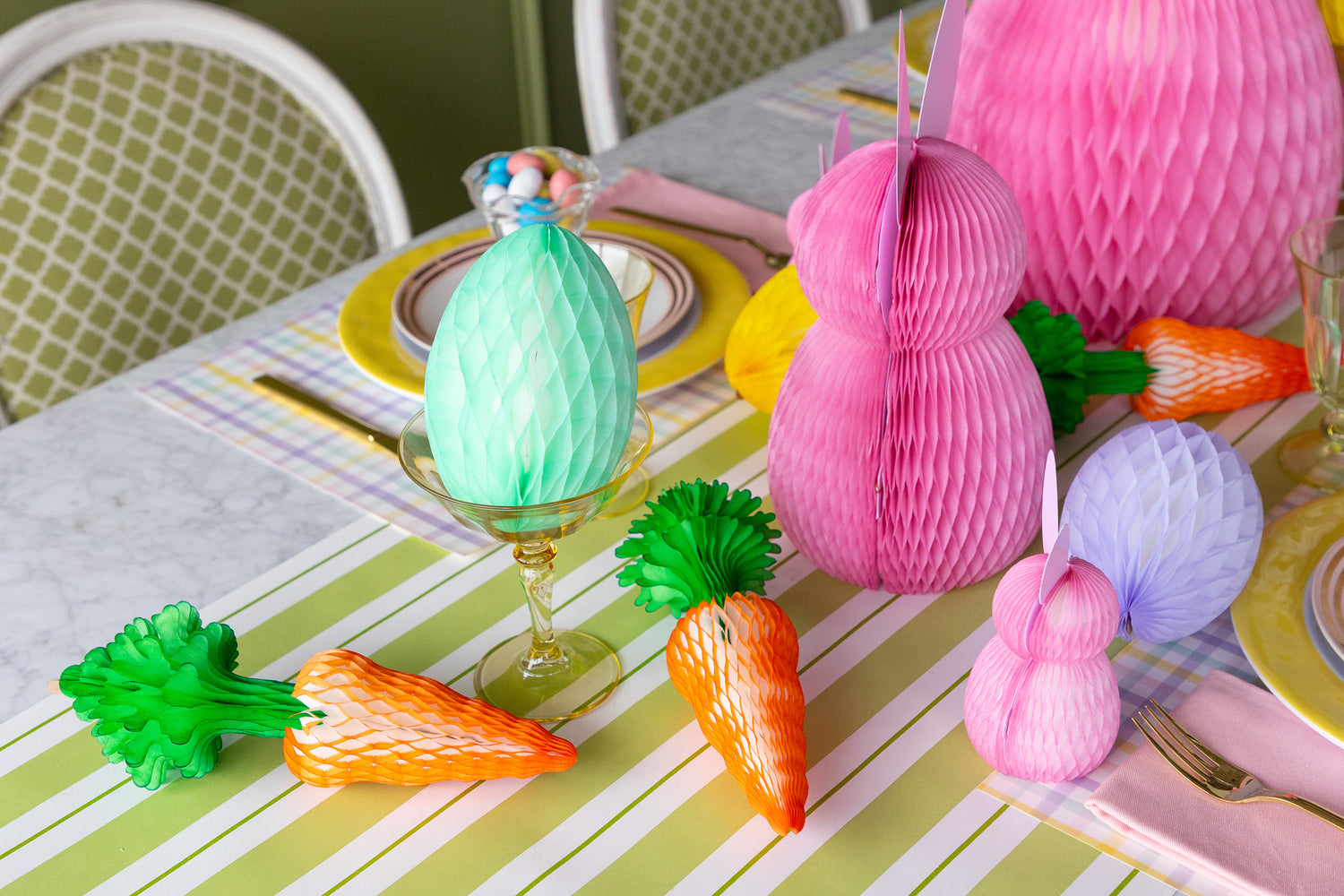 Colorful Easter table setting with paper bunnies, carrots, and eggs on a striped tablecloth.