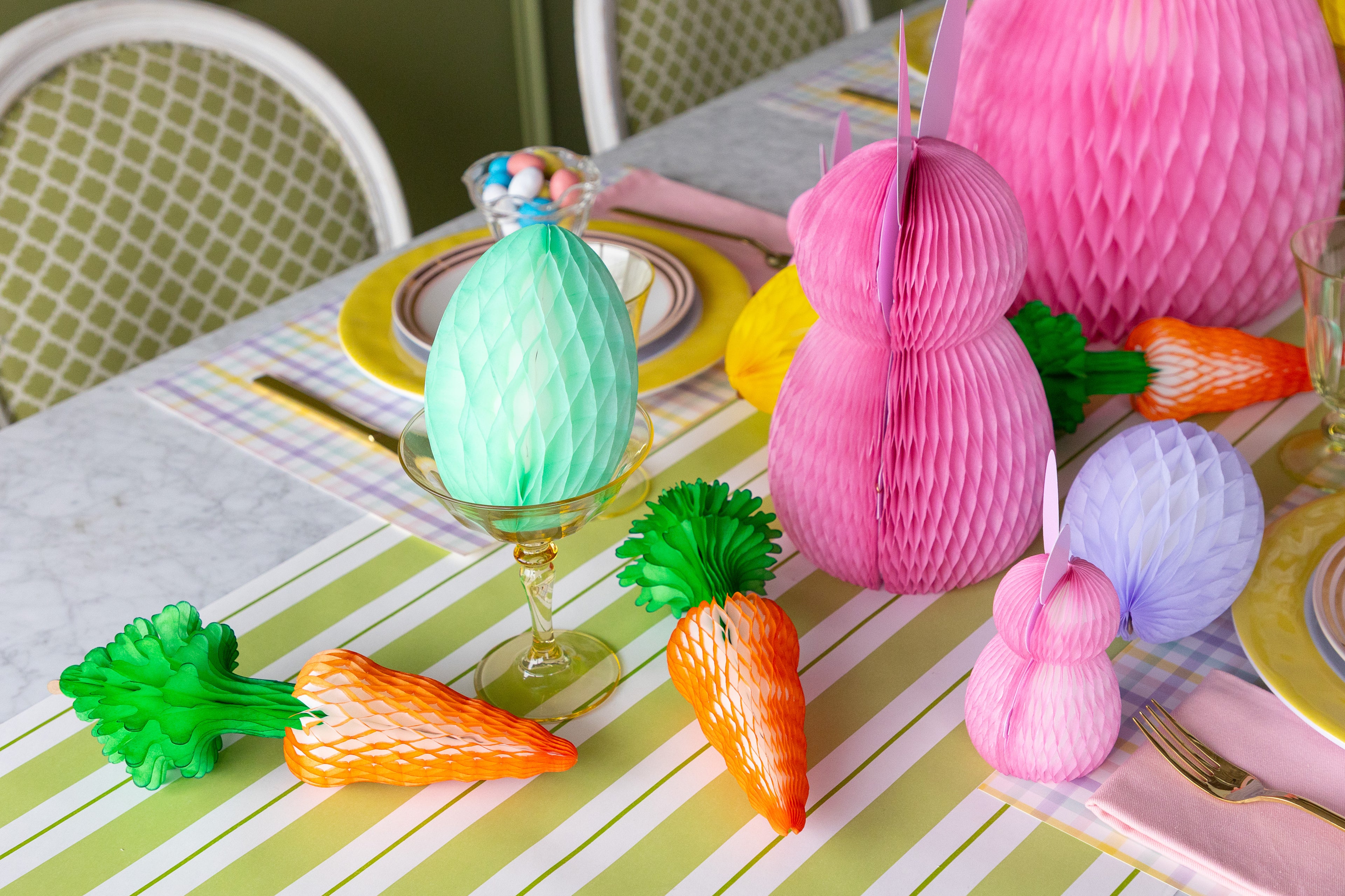 Colorful Easter table setting with paper bunnies, carrots, and eggs on a striped tablecloth.