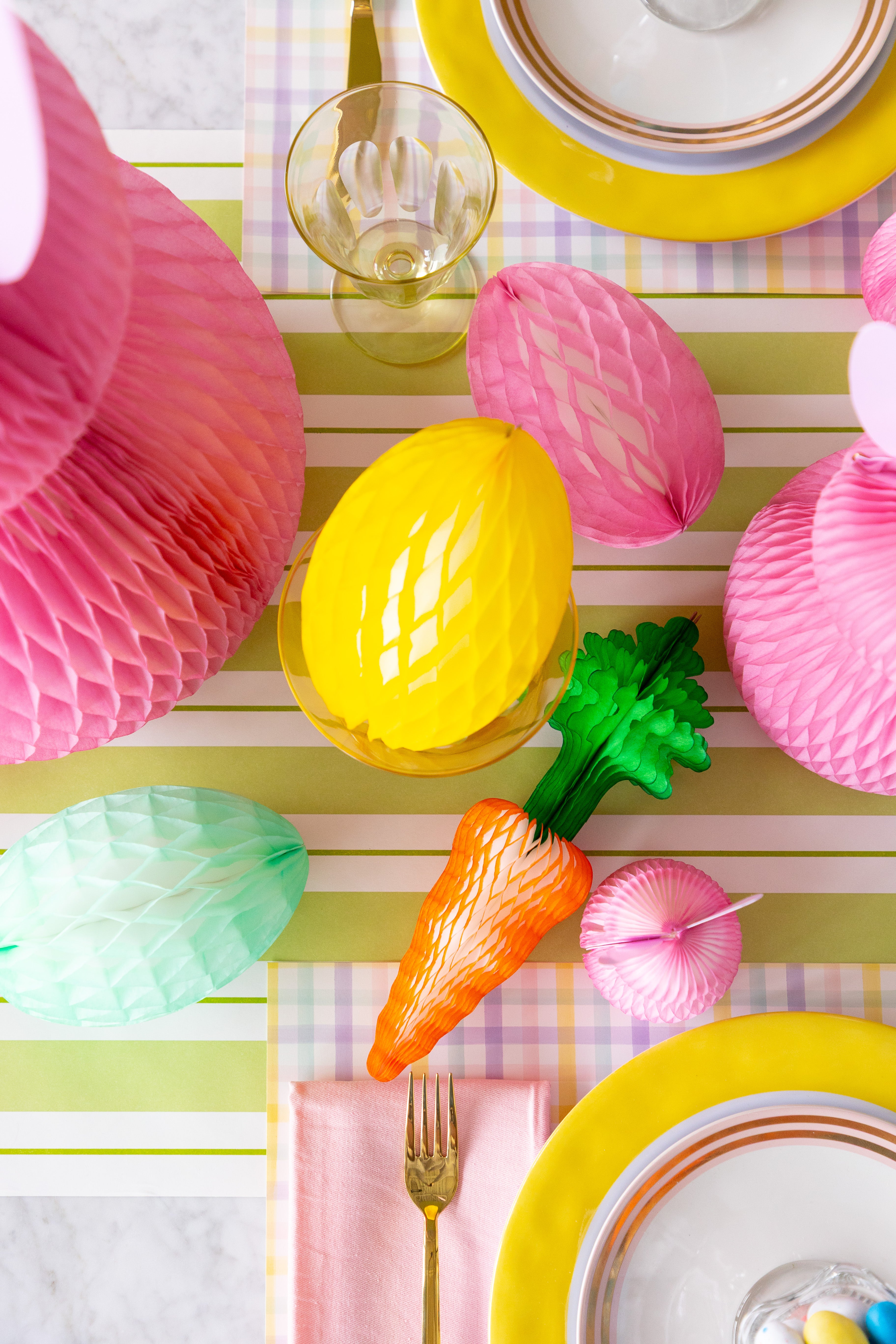 Colorful Easter table setting with pink and yellow decorations on a striped tablecloth.