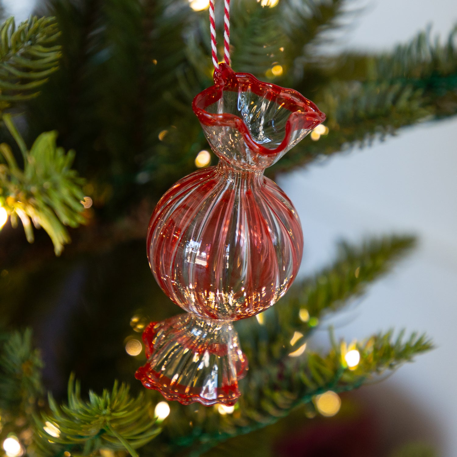 Round, red glass candy shaped ornament hanging on a Christmas tree with lights.
