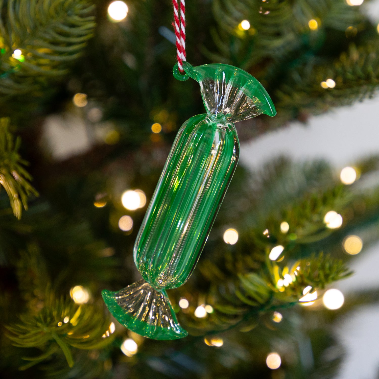 Long green glass candy ornament on a Christmas tree with blurred lights in the background