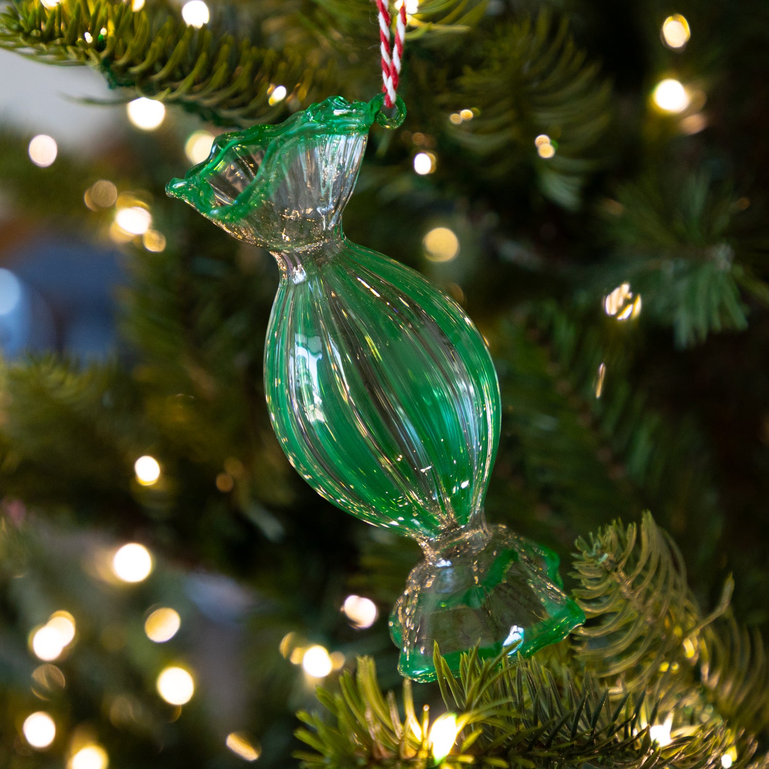Green, round glass candy ornament on a Christmas tree with blurred lights in the background.