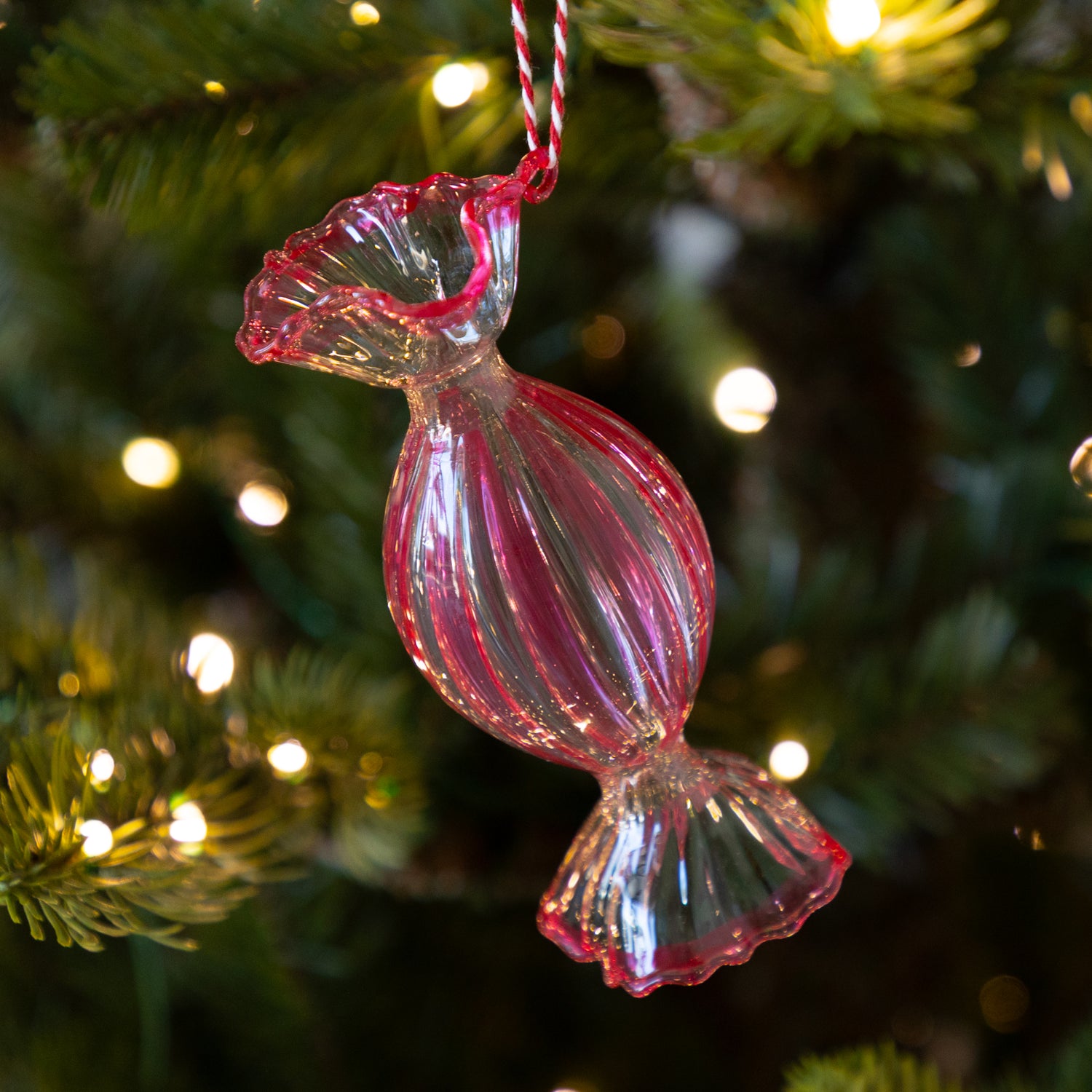 Round, red glass candy ornament hanging on a Christmas tree with lights.