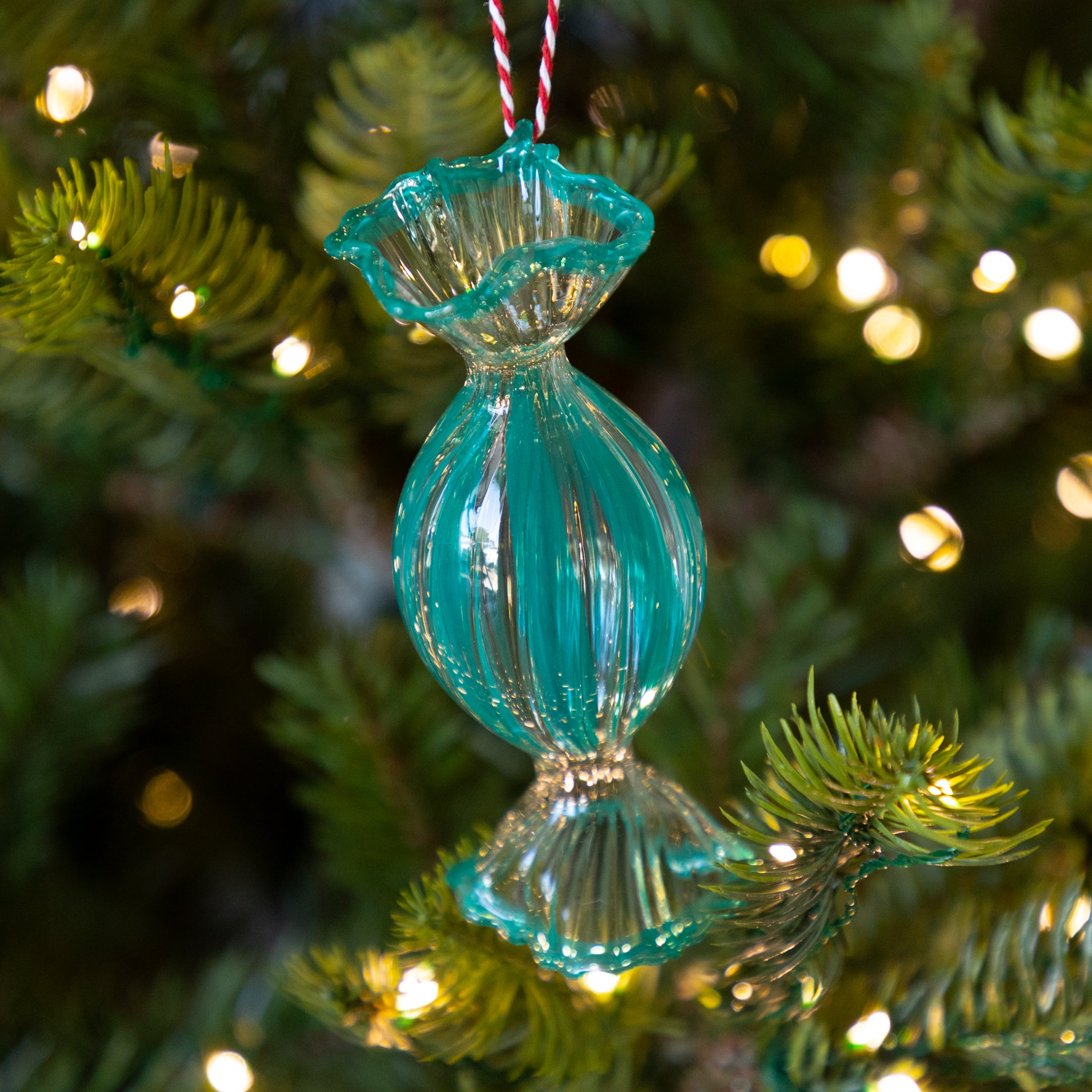 Turquoise, round glass ornament on a Christmas tree with lights in the background.