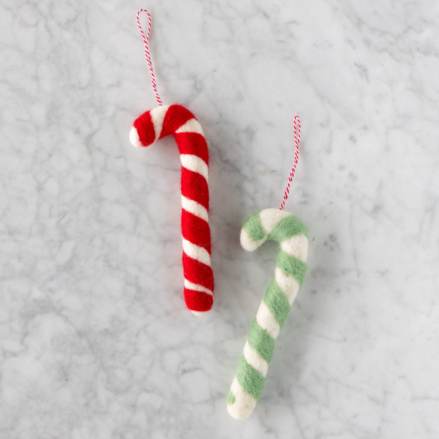 Two felt candy cane-shaped ornaments in red and seafoam on a marble surface.