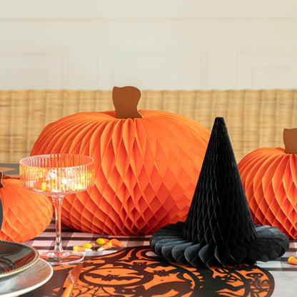 Orange honeycomb pumpkin next to a black honeycomb witch hat, on a Halloween themed table.