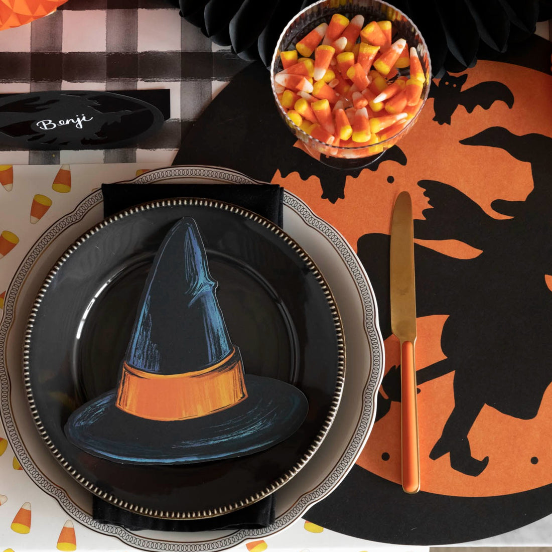 A die-cut black witch hat, with an orange band, on a Halloween themed tablescape.