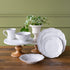 Set of white ceramic dinnerware on a wooden table with a green wall background.