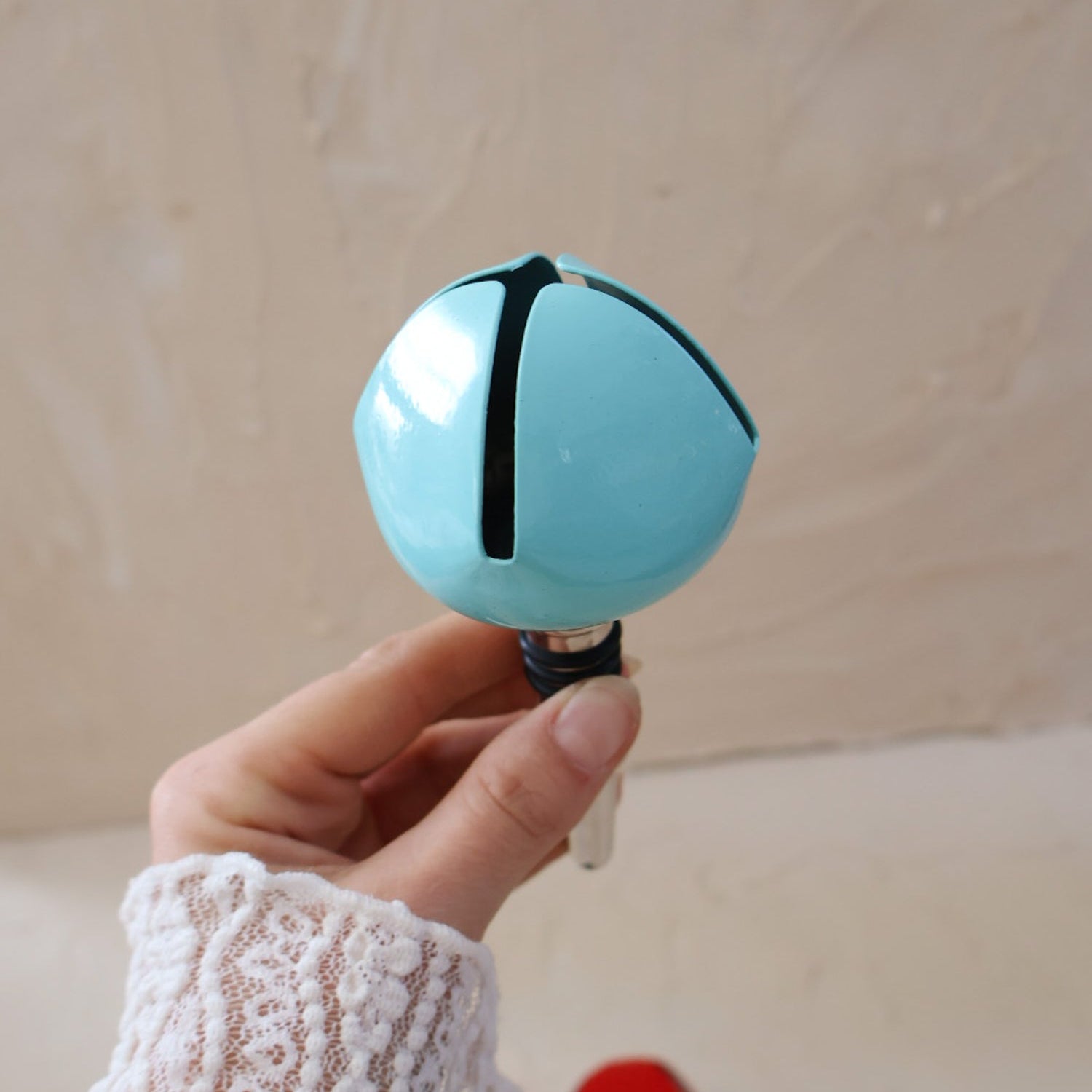 Hand holding a blue bell bottle stopper against a beige background.