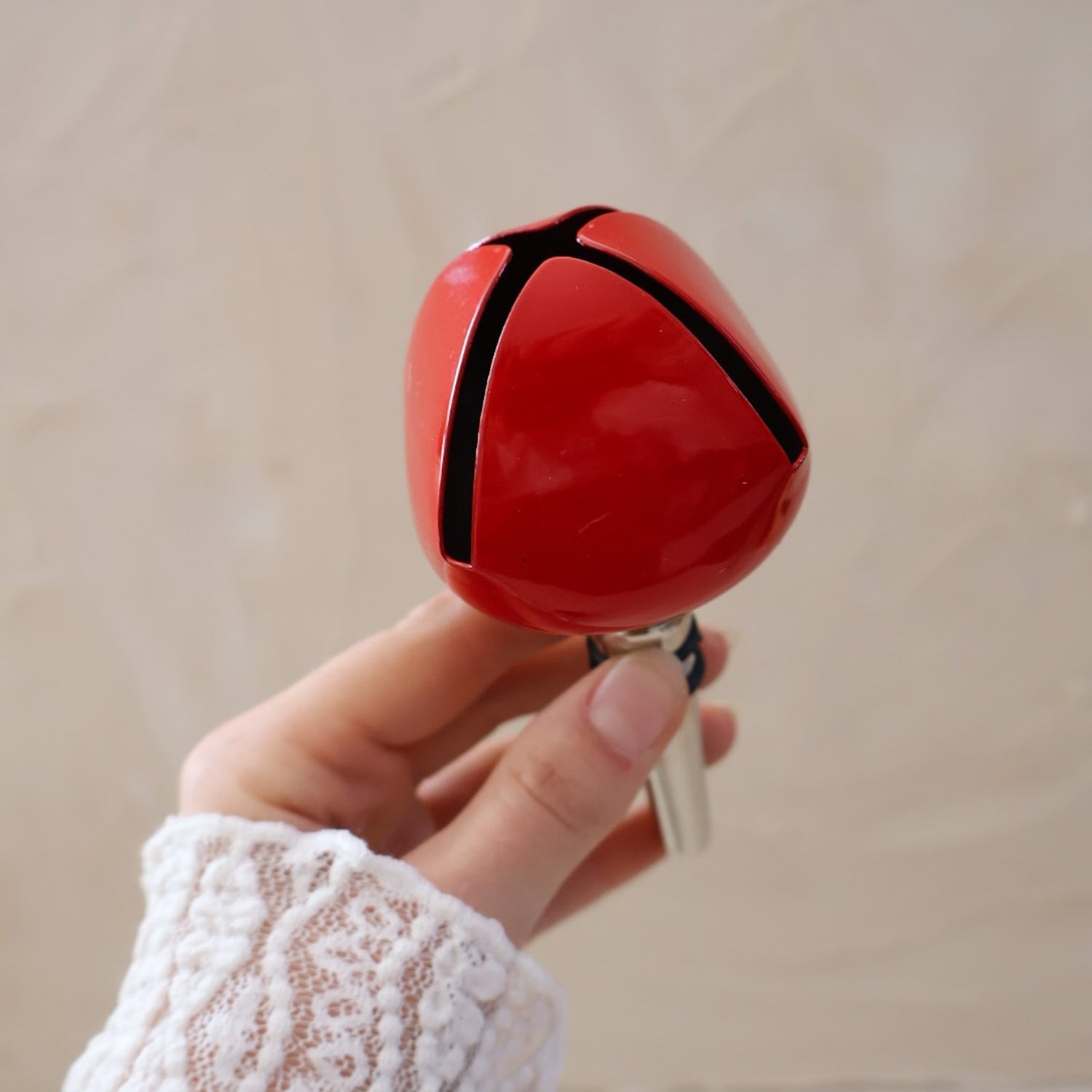 Red bell bottle stopper held by a hand with a white lace sleeve against a beige background.