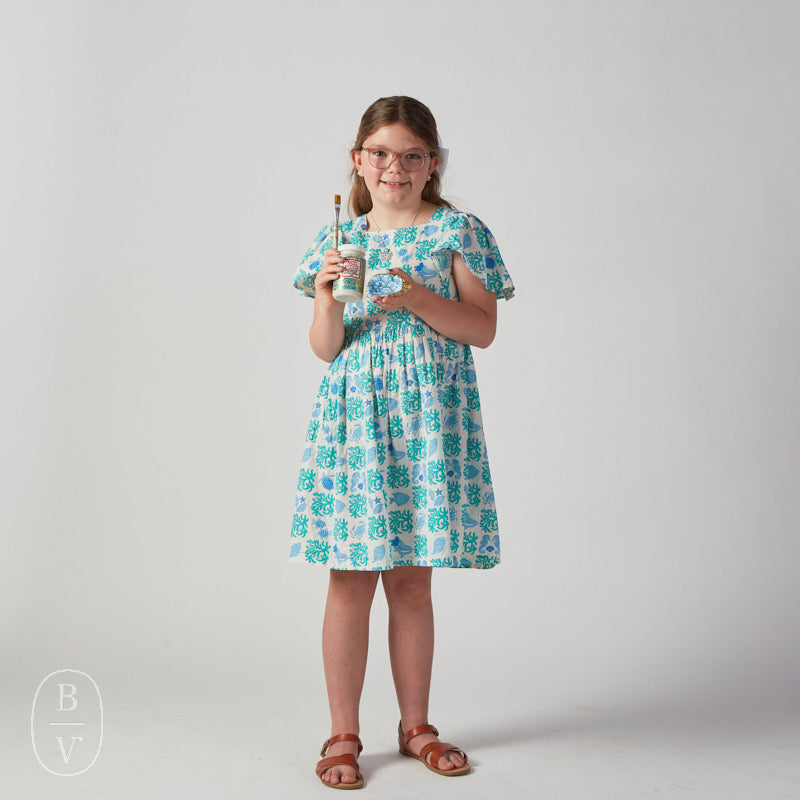 Young girl wearing a floral dress holding mod podge against a plain background.