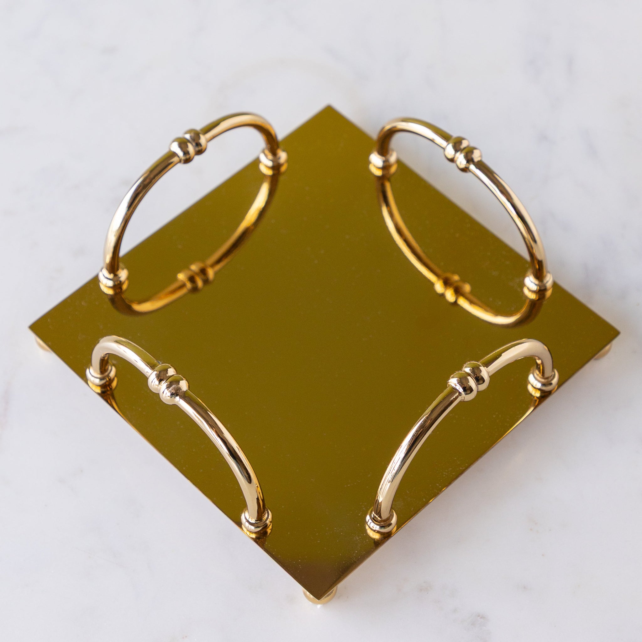 A gold square metal napkin holder with four arched handles sits on a white marble surface.