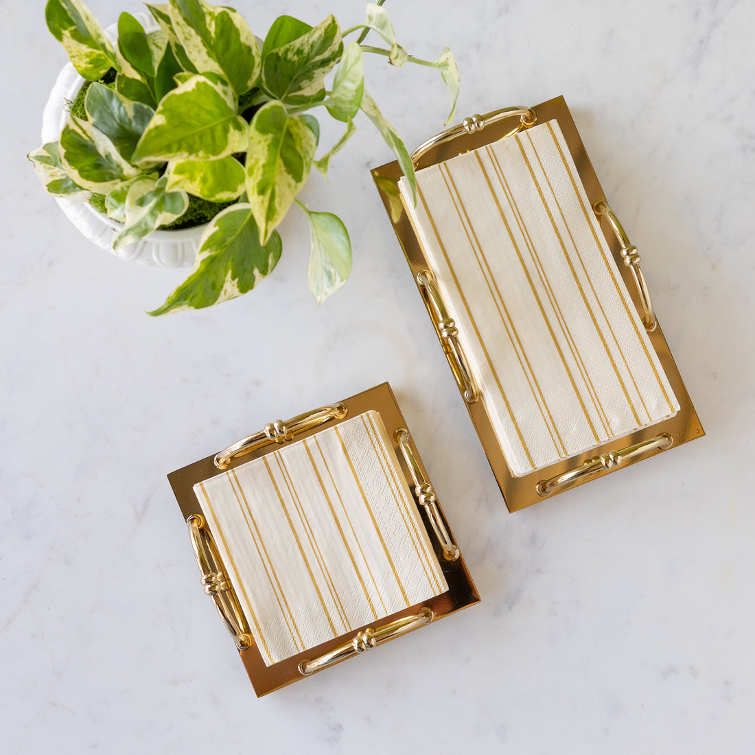 Gold Scalloped Napkin Holders with Antique Gold Stripe Napkins in them, on a marble table with a potted plant.