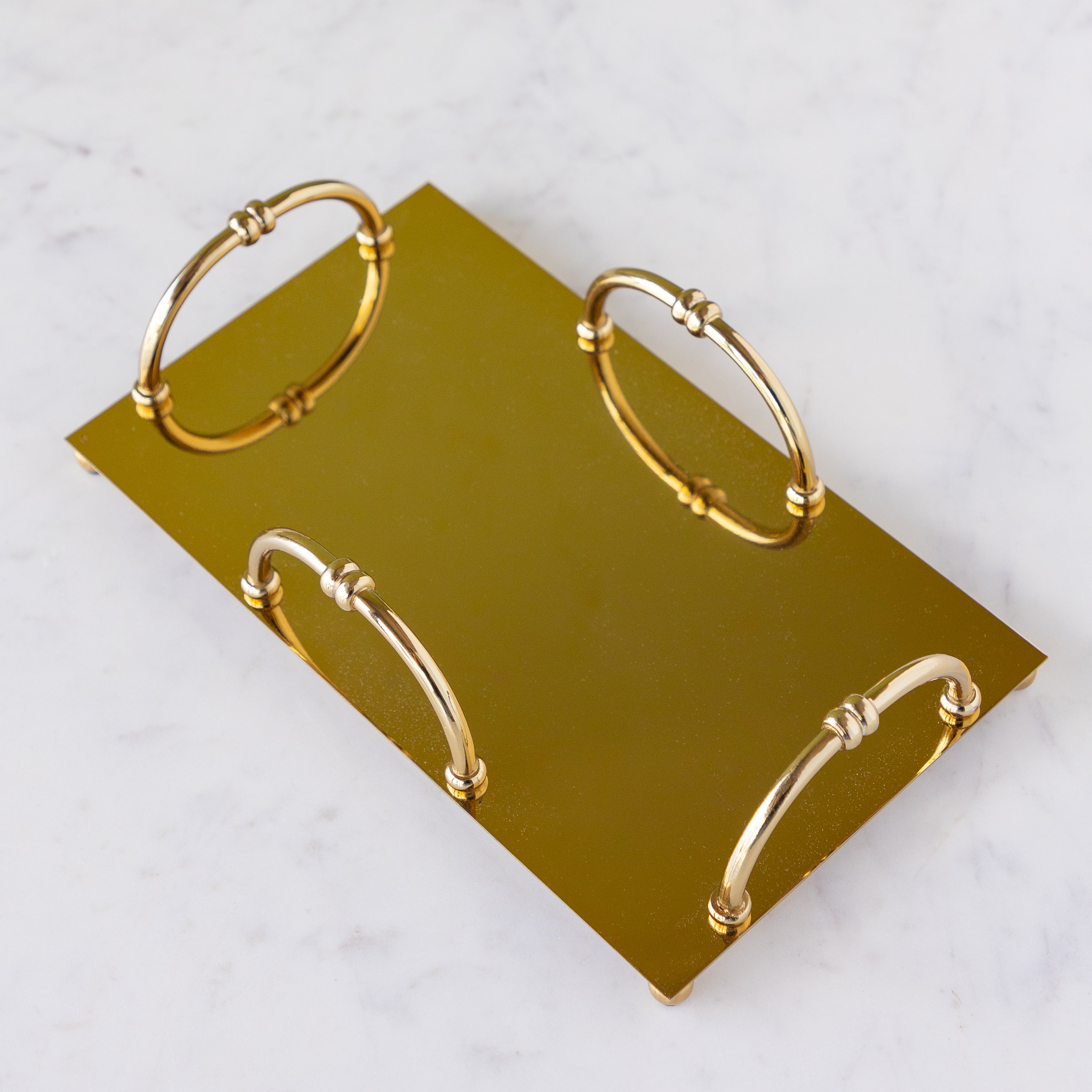 A gold rectangular metal napkin holder with four arched handles sits on a white marble surface.