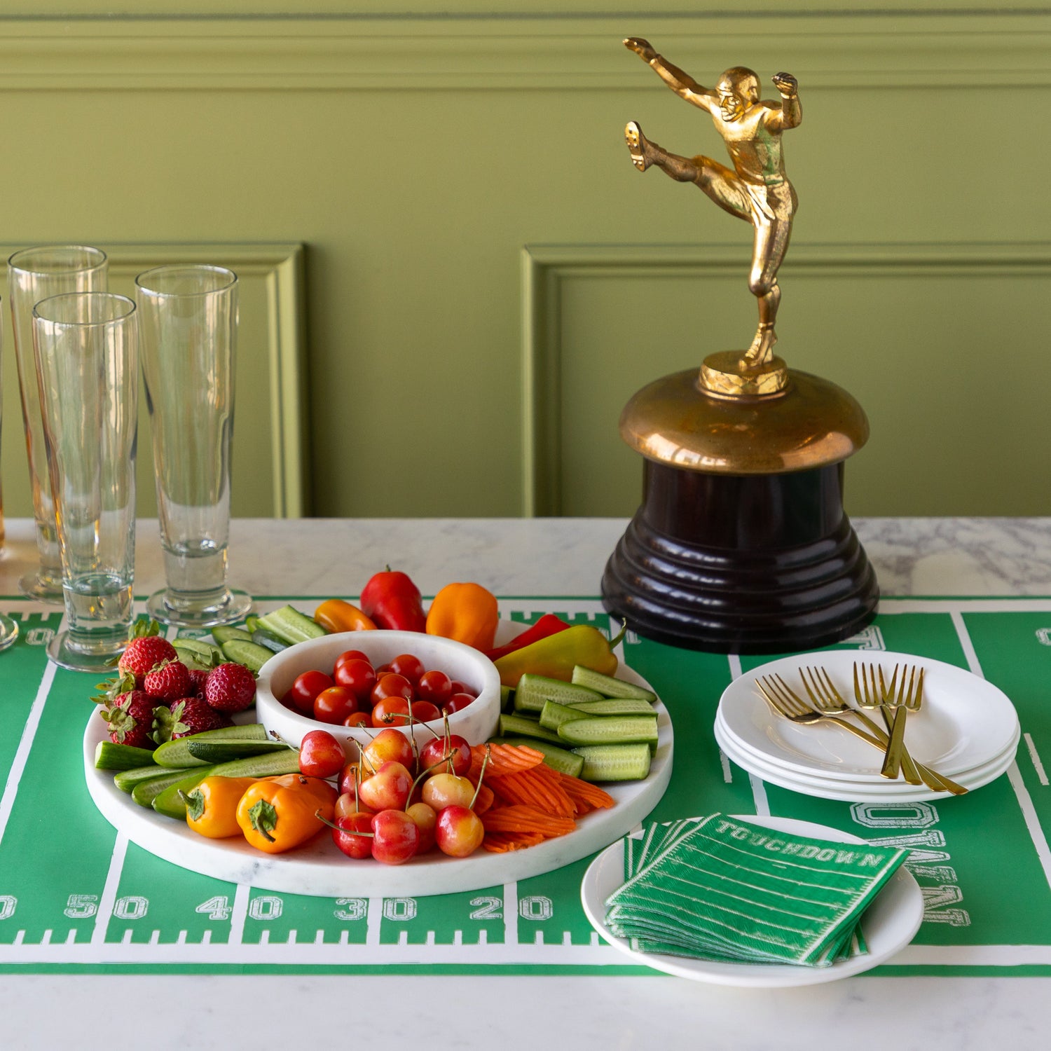 Marble Chip and Dip Server with fruits and veggies atop, Touchdown Cocktail Napkins, a gold trophy, and glasses, plates and forks on the Touchdown Runner.