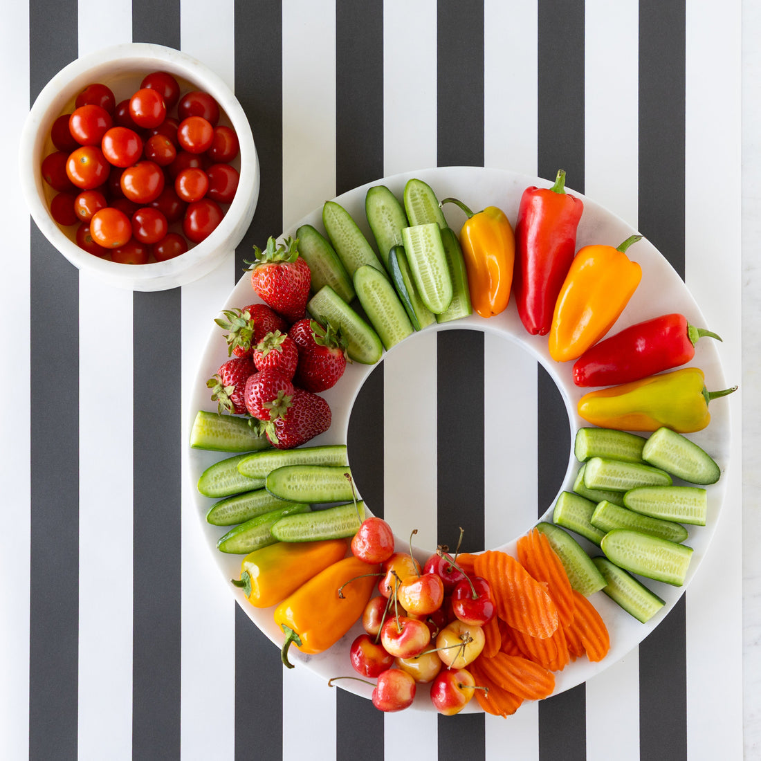 Assorted fruits and vegetables arranged on Marble Chip and Dip Server next to a bowl of cherry tomatoes on the Black Classic Stripe Runner.