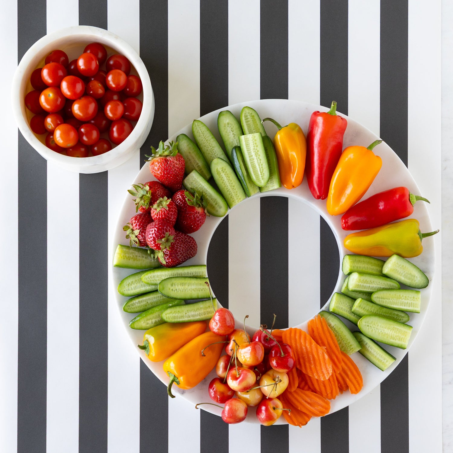 Assorted fruits and vegetables arranged on Marble Chip and Dip Server next to a bowl of cherry tomatoes on the Black Classic Stripe Runner.