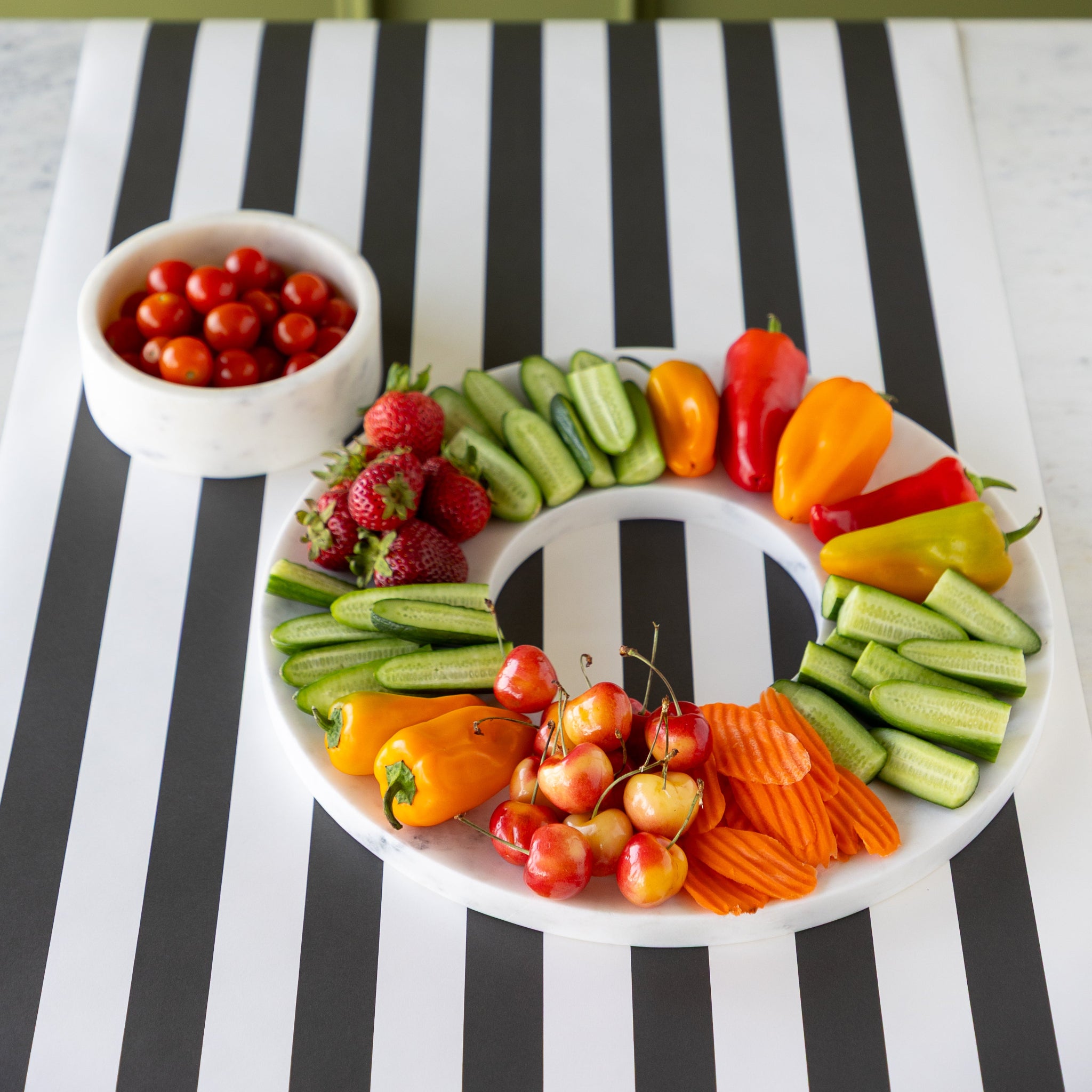 Assorted fruits and vegetables on the Marble Chip and Dip Server next to the bowl of cherry tomatoes, on the Black Classic Stripe Runner.