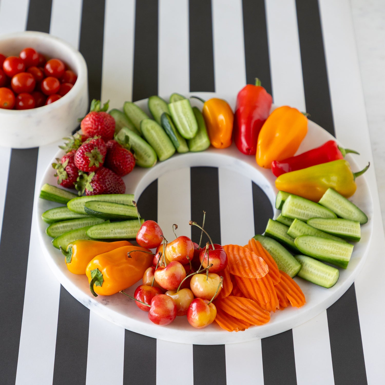 Assorted fruits and vegetables on the Marble Chip and Dip Server next to the bowl of cherry tomatoes, on the Black Classic Stripe Runner.