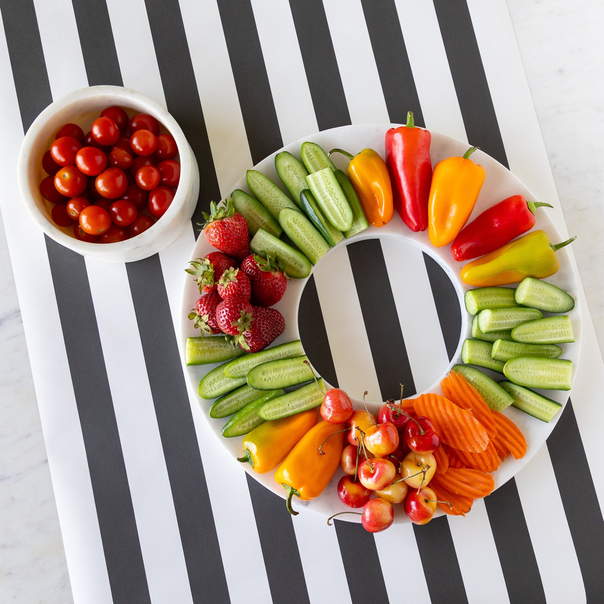 Assorted fruits and vegetables on the Marble Chip and Dip Server next to the bowl of cherry tomatoes, on the Black Classic Stripe Runner.
