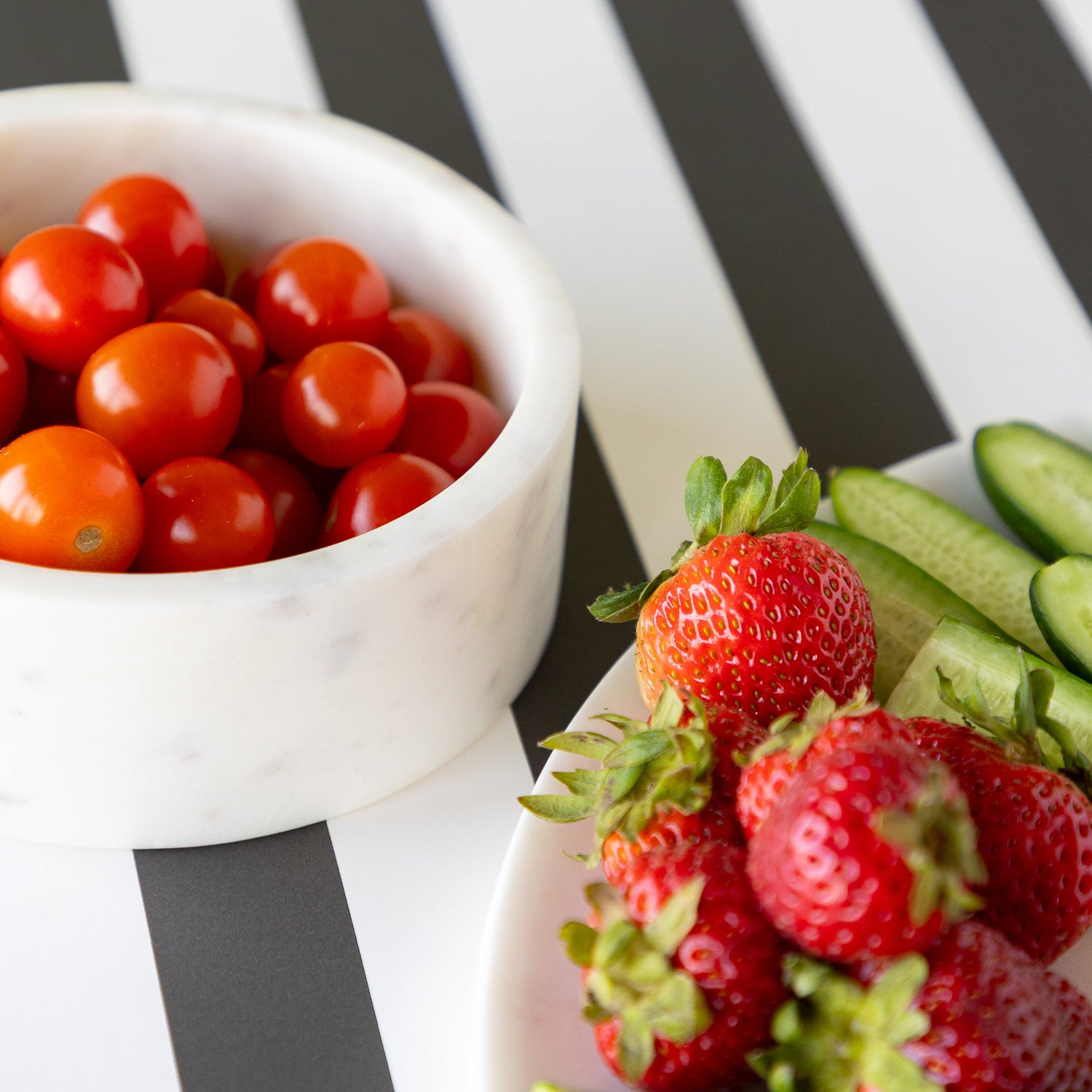 Bowl of cherry tomatoes next to the Marble Chip and Dip Server plate with strawberries and cucumbers.