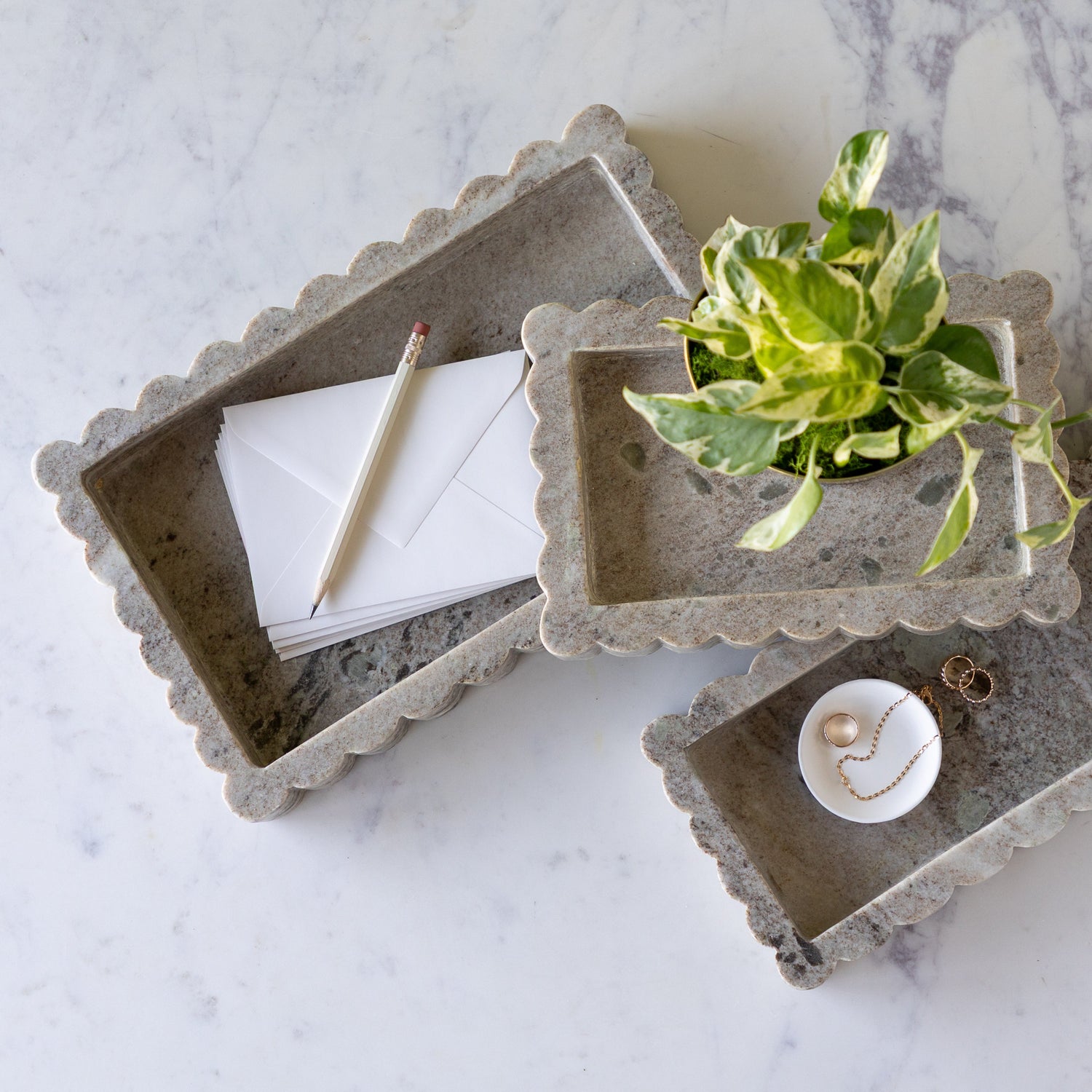 Intricate Scallop Marble Trays in 3 sizes with a potted plant in the small, trinket dish with jewelry in the medium and envelopes and a pencil in the large.