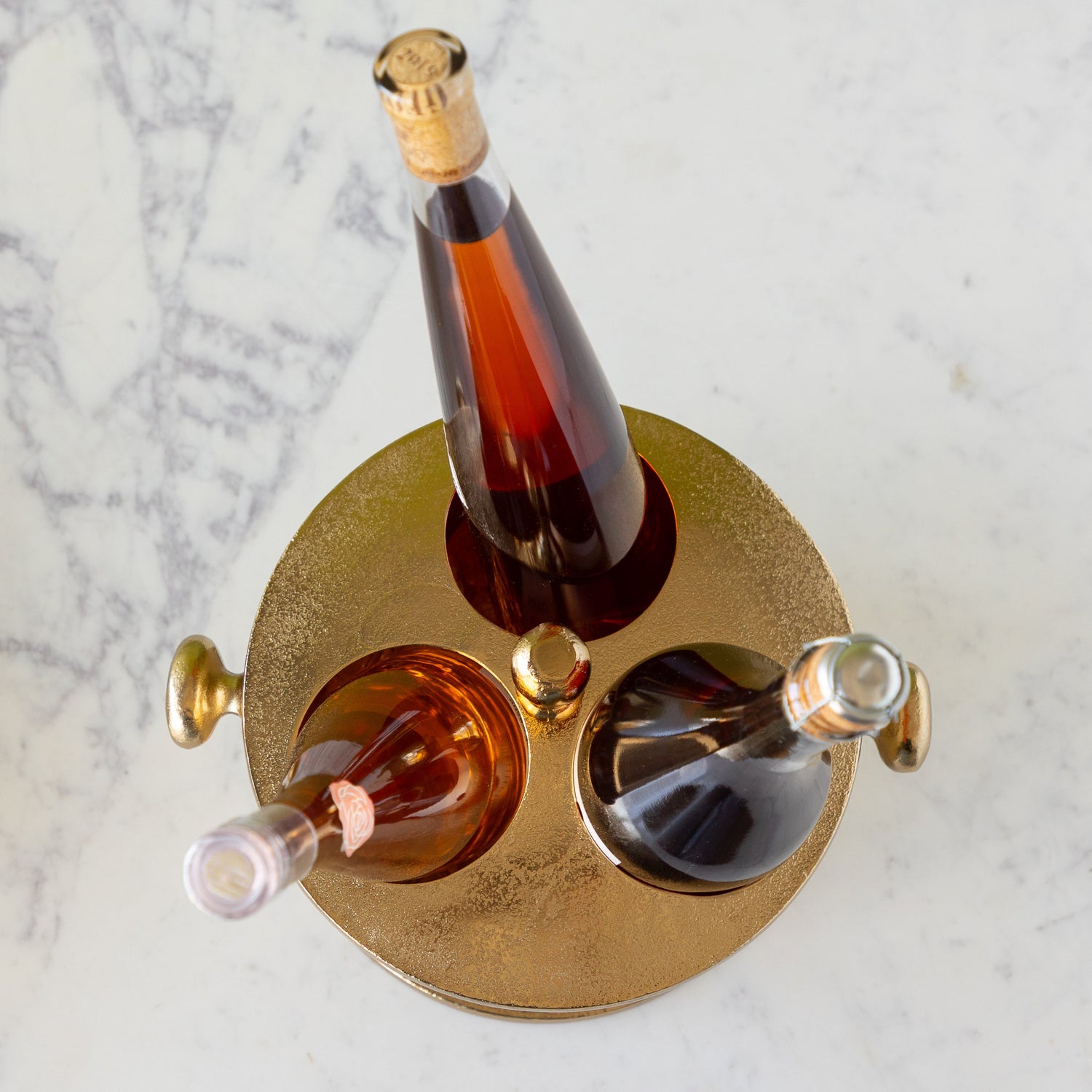 Three bottles of alcohol in the Gold Raw Aluminum Bottle Holder.