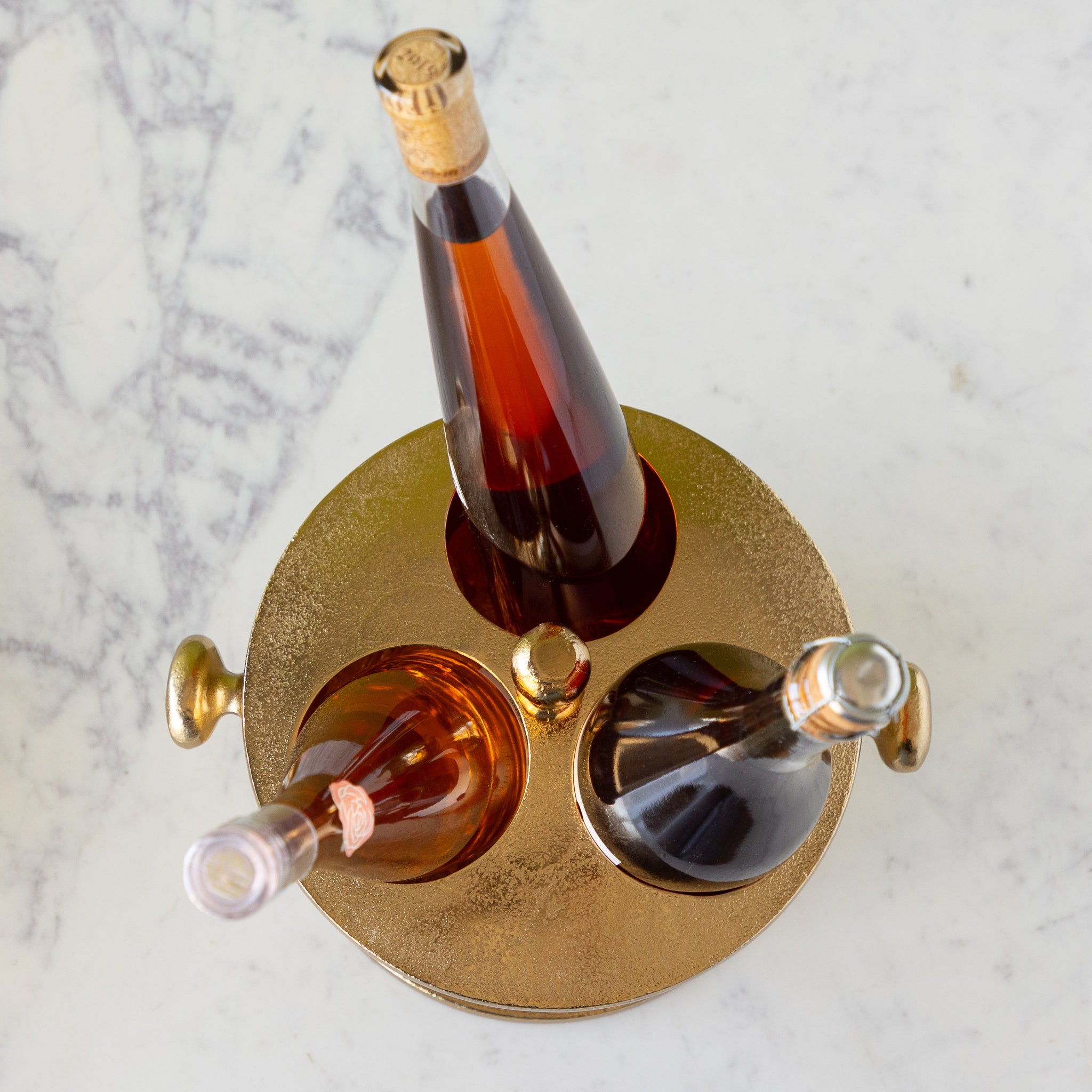 Three bottles of alcohol in the Gold Raw Aluminum Bottle Holder.