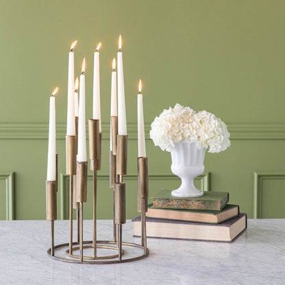 One short iron taper candle holder nestled inside of a tall iron taper candleholder, with various heights of lit candles, on a table with flowers stacked on top of books.