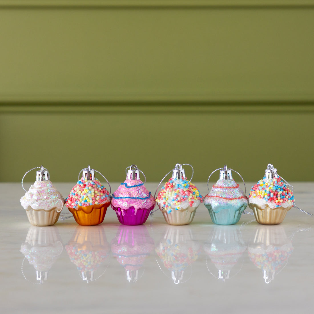 Colorful cupcake-shaped ornaments on a marble surface with a green wall background.