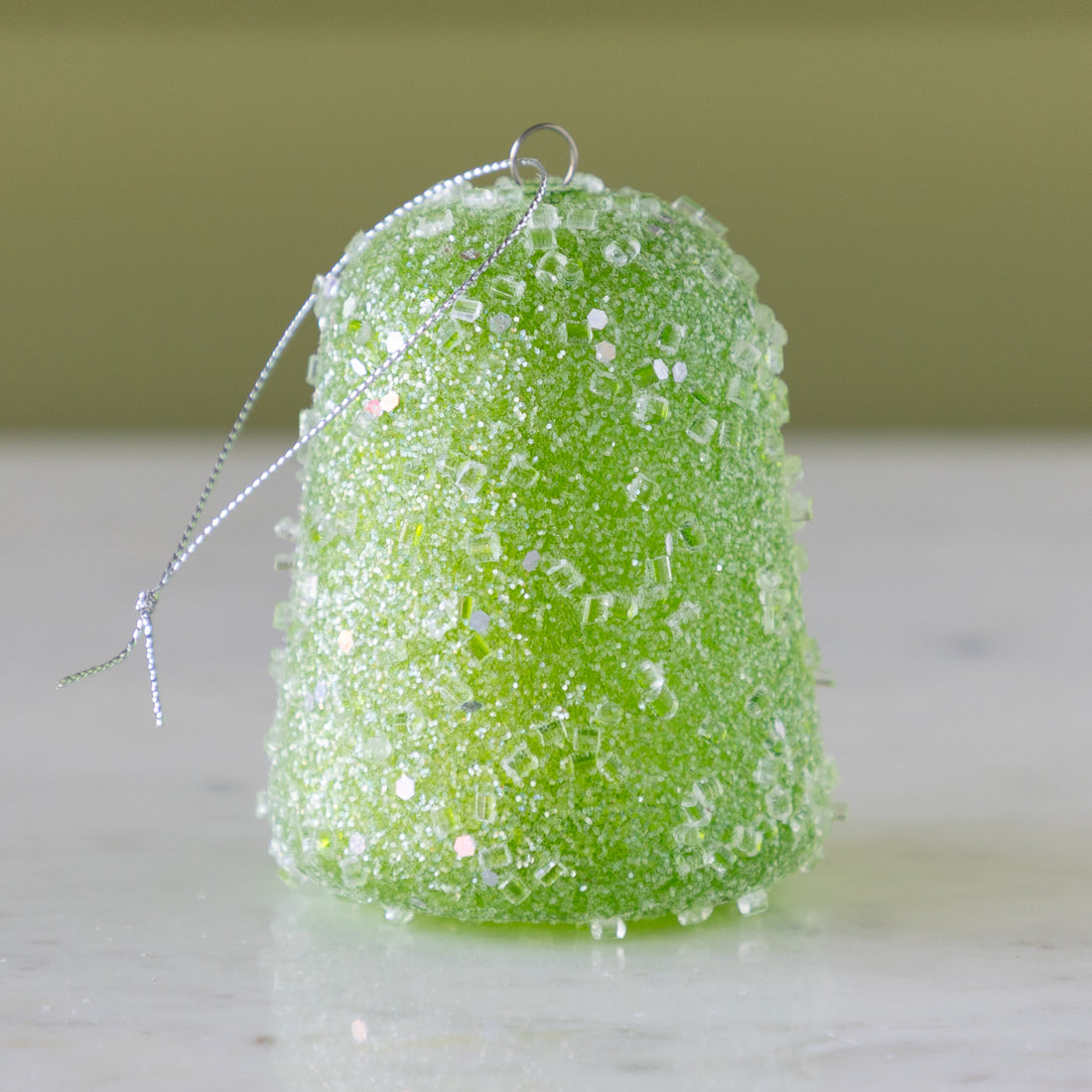 Green glittery gum drop ornament on a neutral background.
