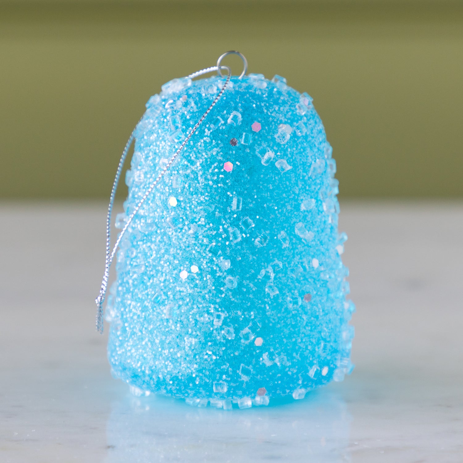 Blue glittery gum drop ornament on a neutral background.