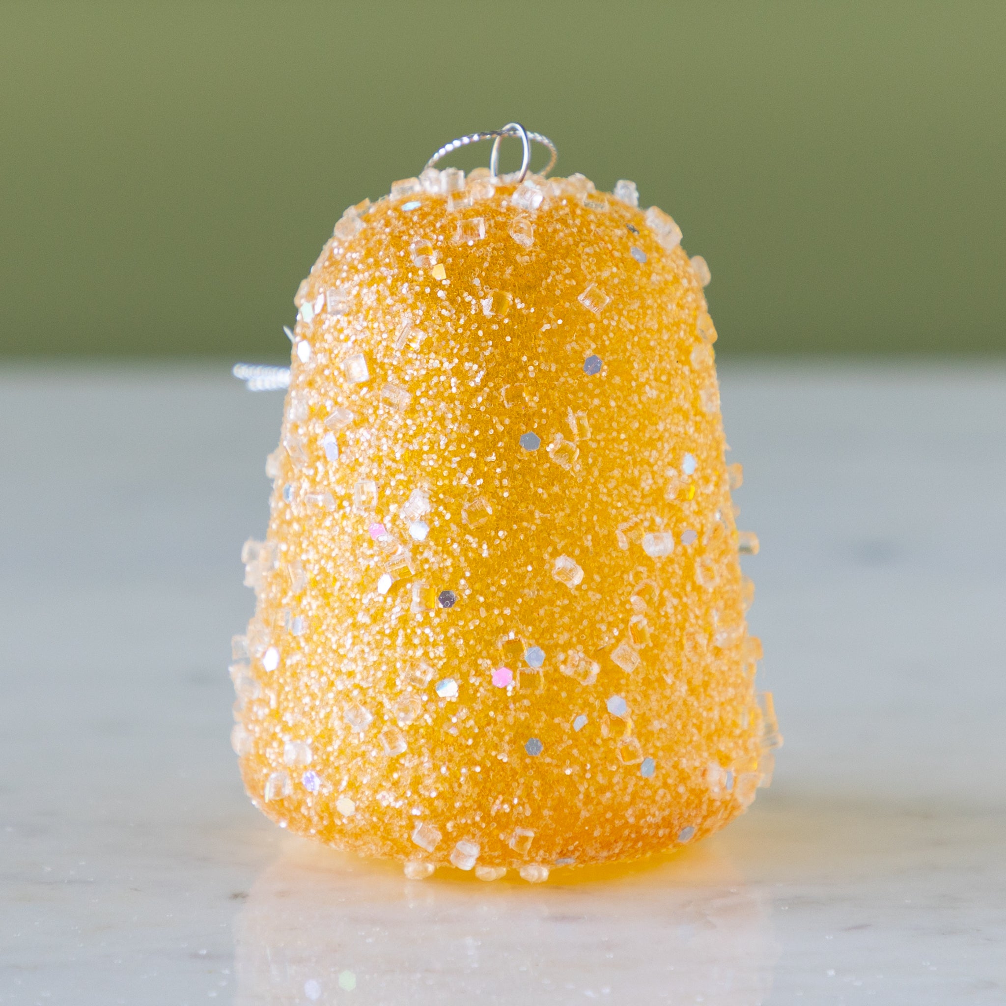 Yellow glittery gum drop ornament on a neutral background.