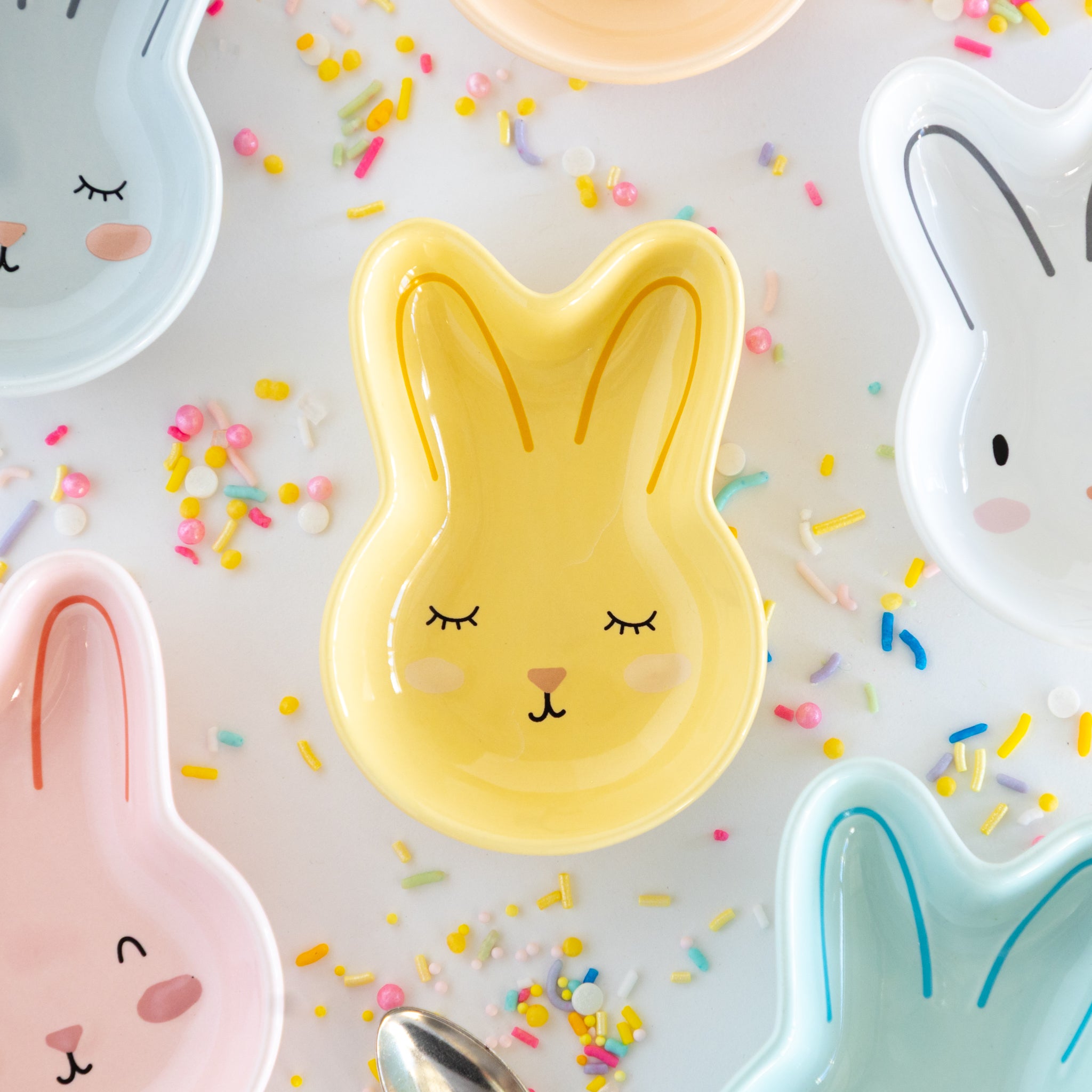 Yellow bunny-shaped dish with closed eyes on a white background with colorful sprinkles.