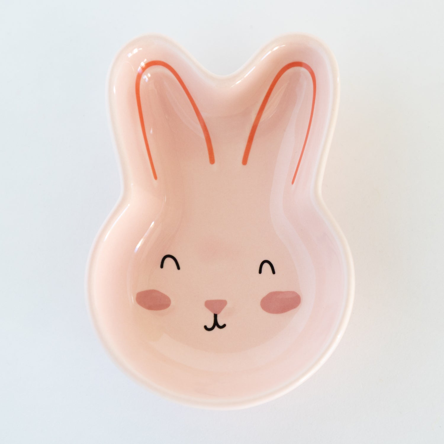 Pink bunny-shaped dish with a face on a light gray background.
