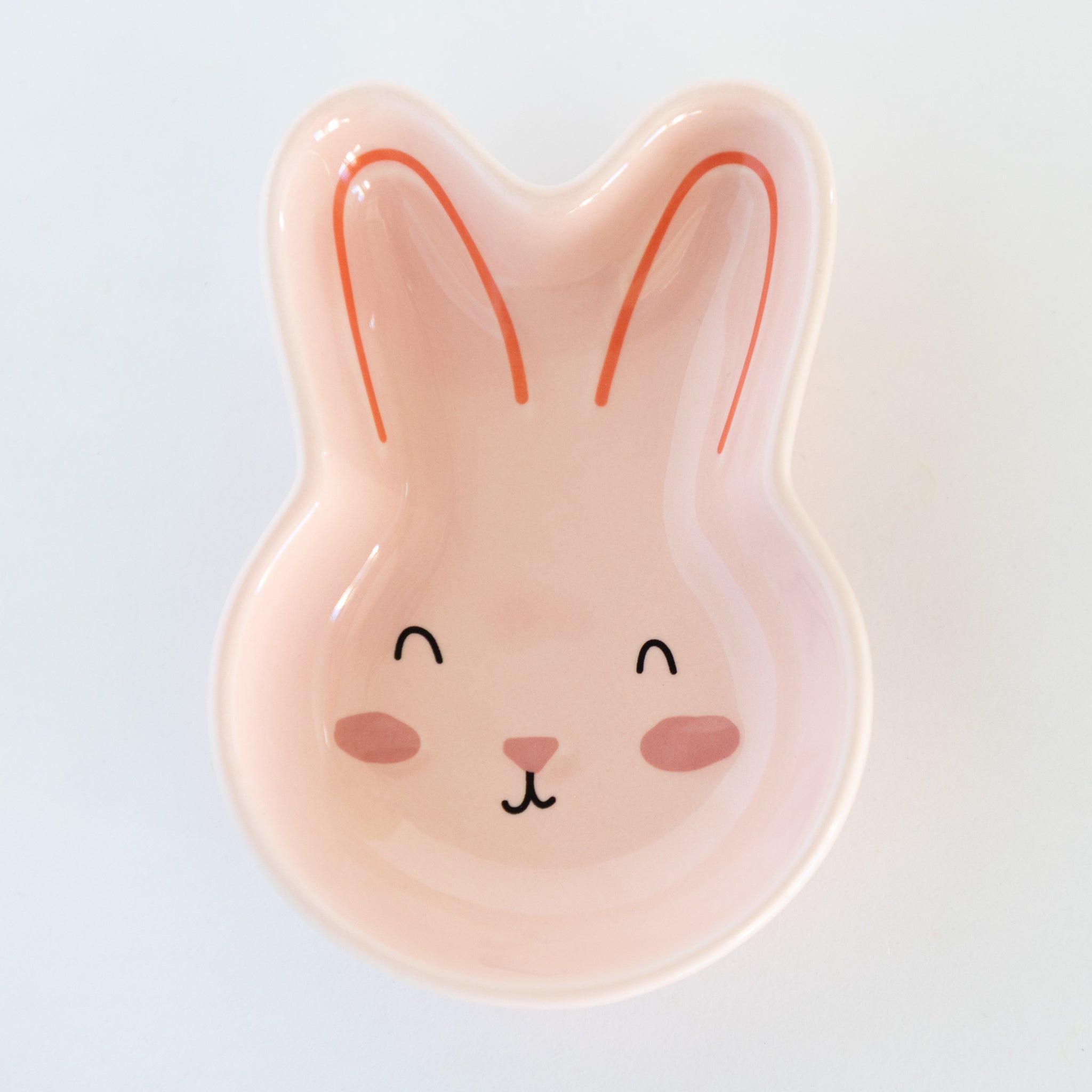 Pink bunny-shaped dish with a face on a light gray background.