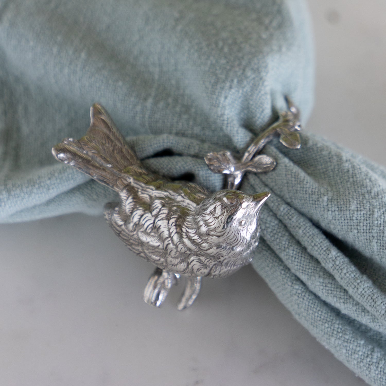 Silver bird-shaped napkin ring on a green napkin.