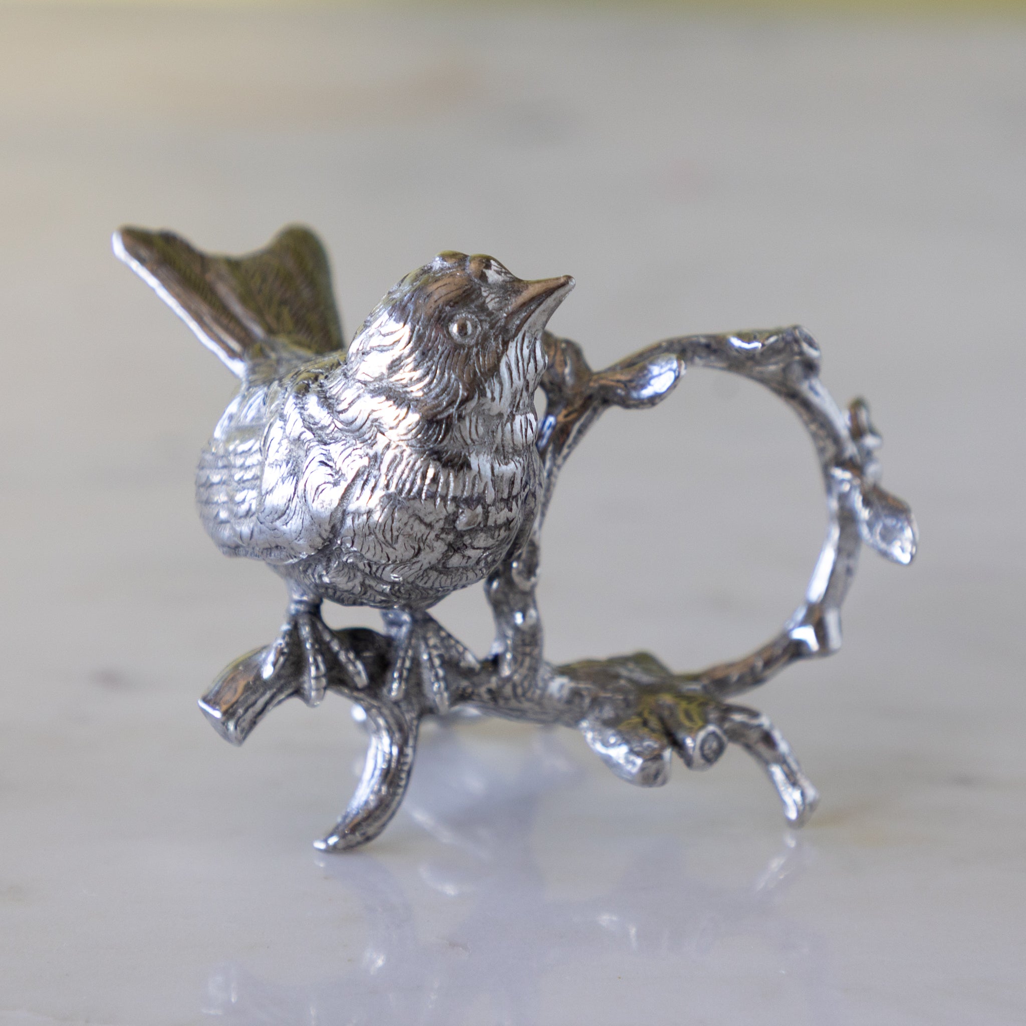 Silver bird a branch with a circular element, on a light background.