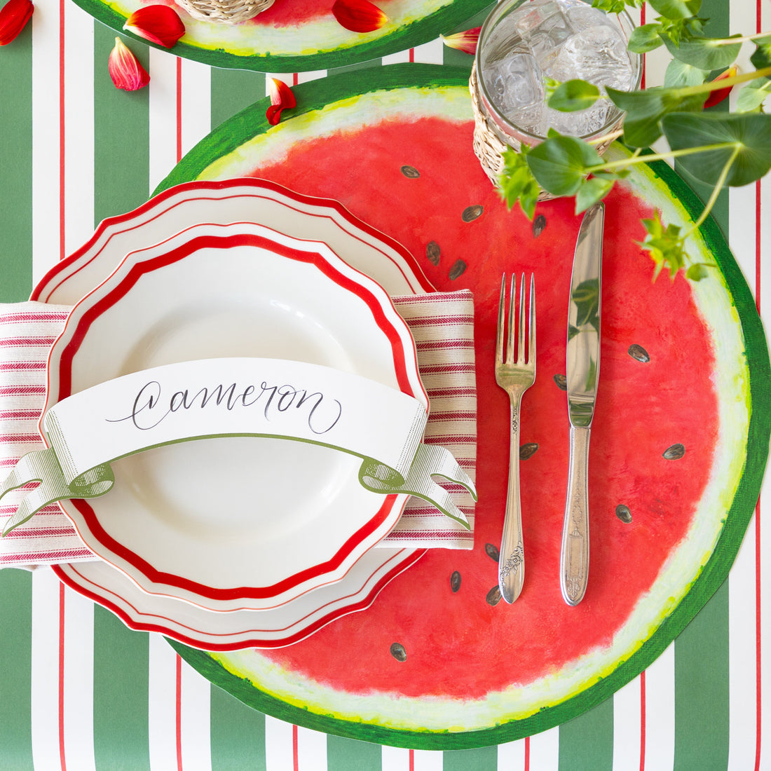 Place setting with the Die-cut Watermelon Placemat, Fancy Red Scalloped Plates, Classic Moss Banner Table Accent and silverware on the Green &amp; Red Awning Stripe Runner.