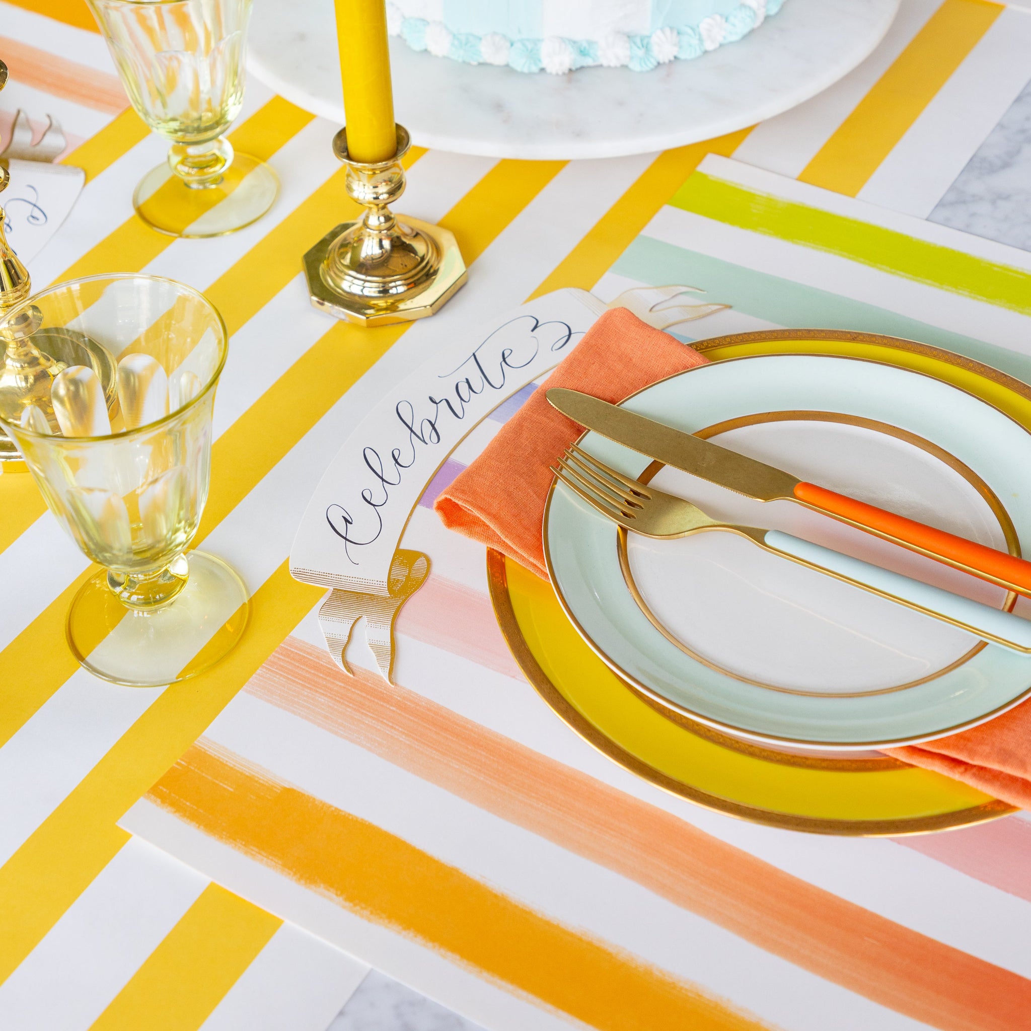 Decorative table setting with a cake, candles, and Sorbet Painted Stripe Placemat on the Marigold Classic Stripe Runner.