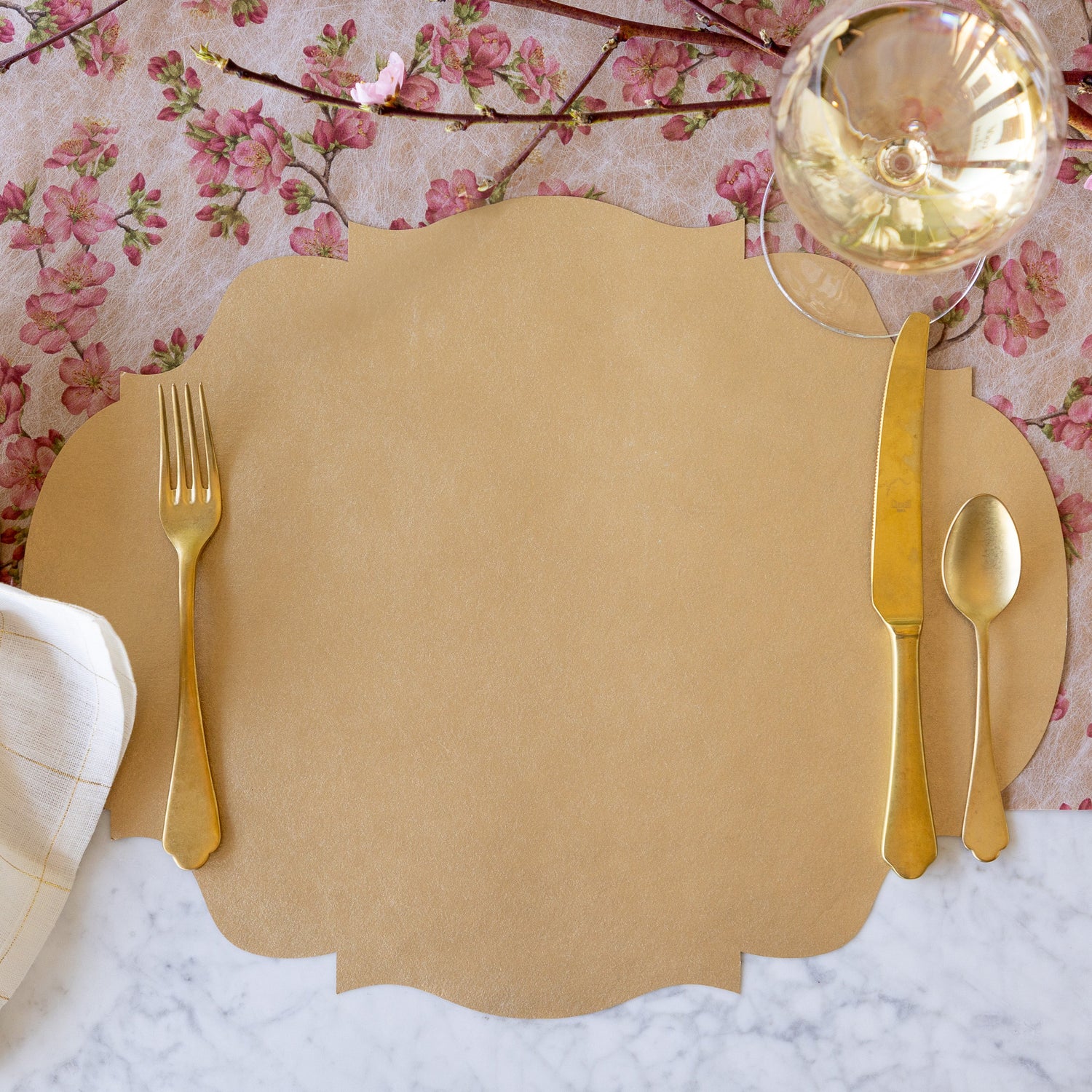 A place setting featuring the Die-cut Gold French Frame Placemat under gold flatware and a glass of wine, with the Cherry Blossom Runner underneath.
