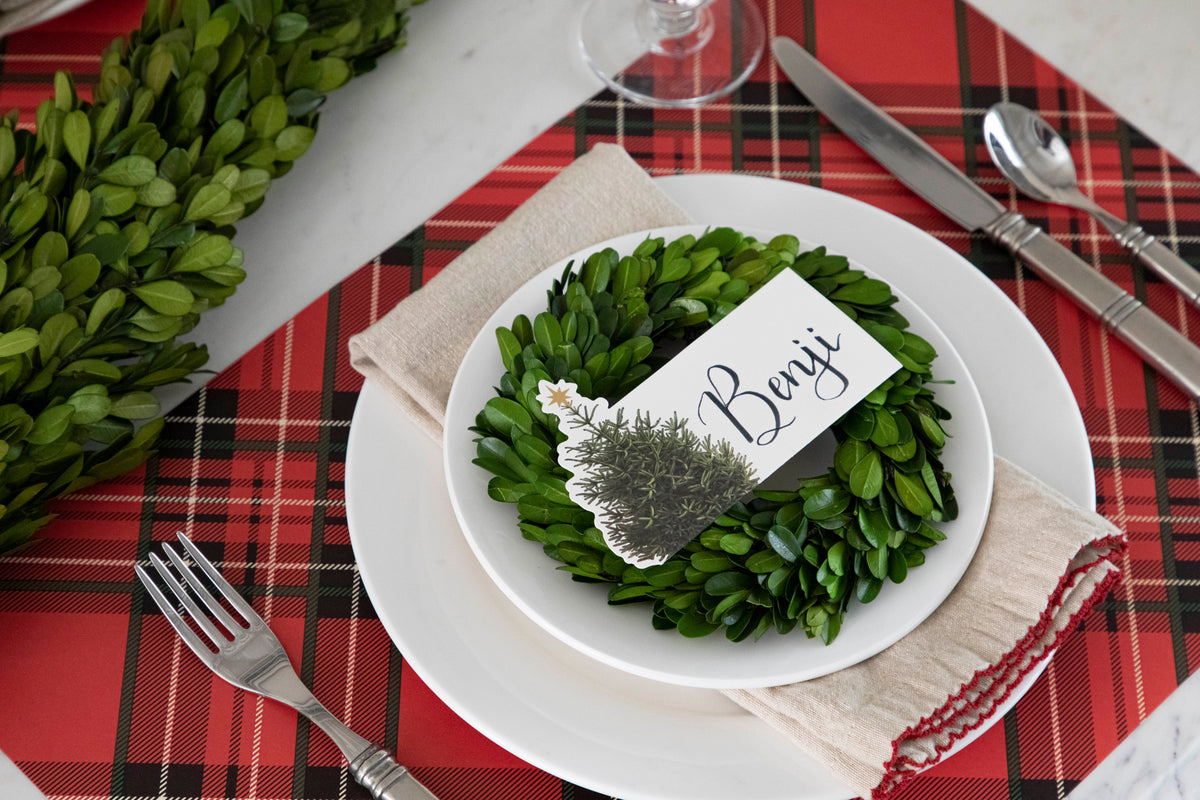 An elegant Christmastime place setting, featuring a Christmas Tree Place Card labeled &quot;Benji&quot; laying flat on the plate.