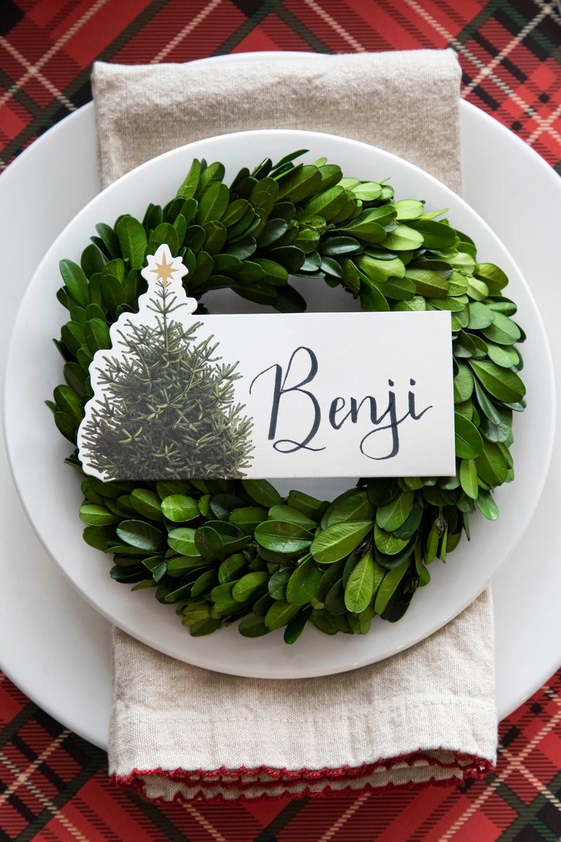 Top-down view of an elegant Christmastime place setting, featuring a Christmas Tree Place Card labeled &quot;Benji&quot; laying flat on the plate.