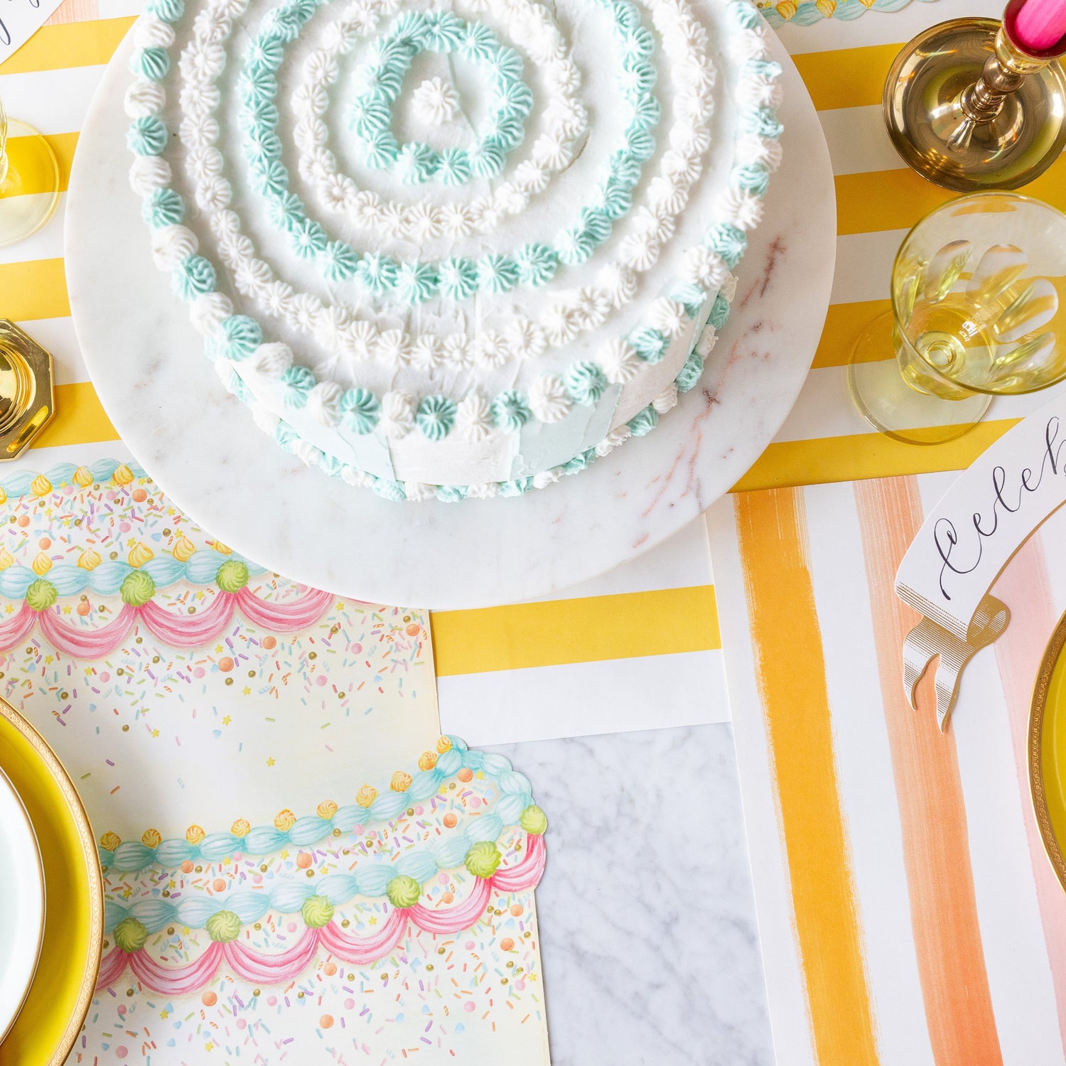 A colorful table setting featuring the Die-cut Birthday Cake Placemat, Sorbet Painted Stripe Placemat and decorative cake on the Marigold Classic Stripe Runner.