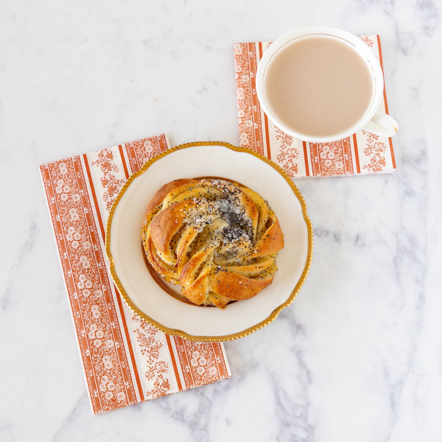 The Pumpkin Burleigh Stripe Cocktail Napkin under a cup of coffee and the Pumpkin Burleigh Stripe Guest Napkin under a plate with a decadent croissant.