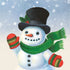An illustration of a snowman with a carrot nose and coal eyes and mouth, wearing a black top hat adorned with holly, a green scarf and festive mittens, in a snowy scene.