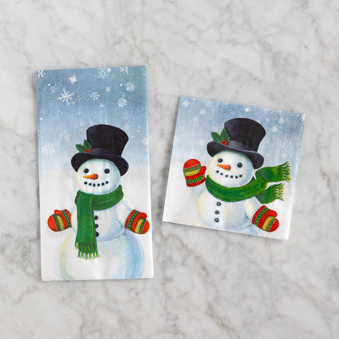 Two snowman-themed napkins with a winter background on a marble surface.